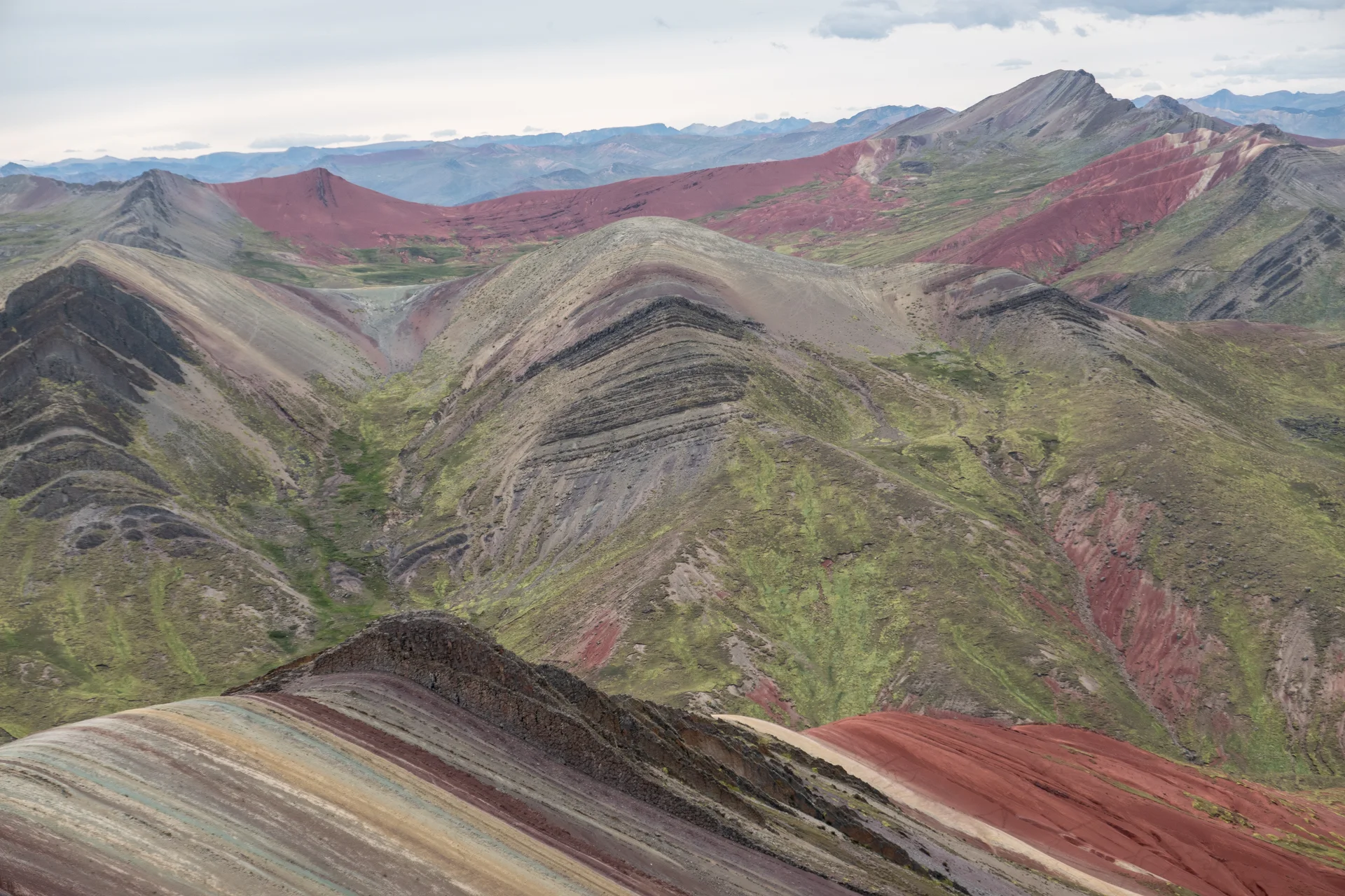 Colourful ridges at Palccoyo, with red rock and green vegetation between the slopes.