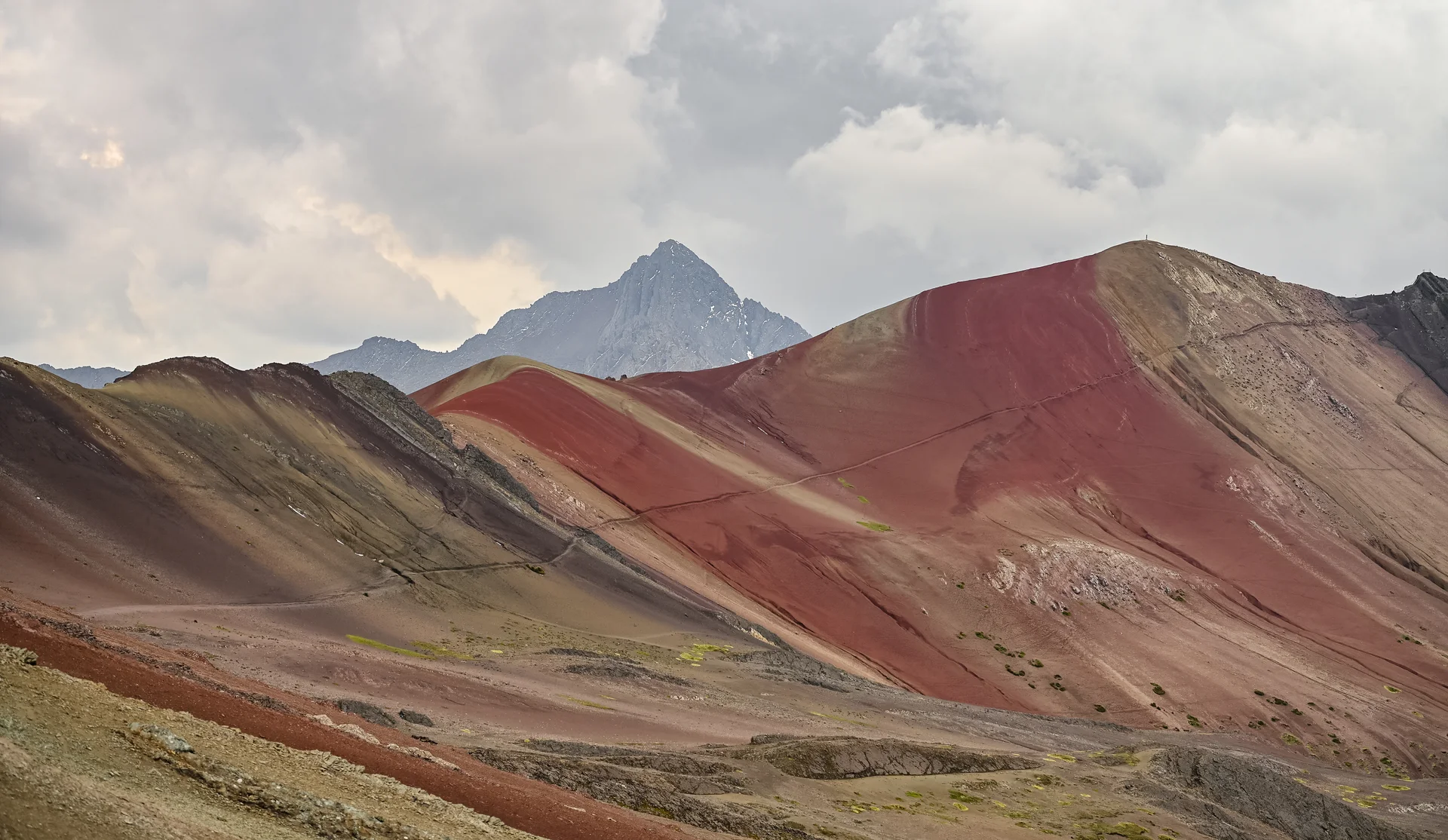 Red and ochre slopes at Vinicunca beneath a cloudy sky.